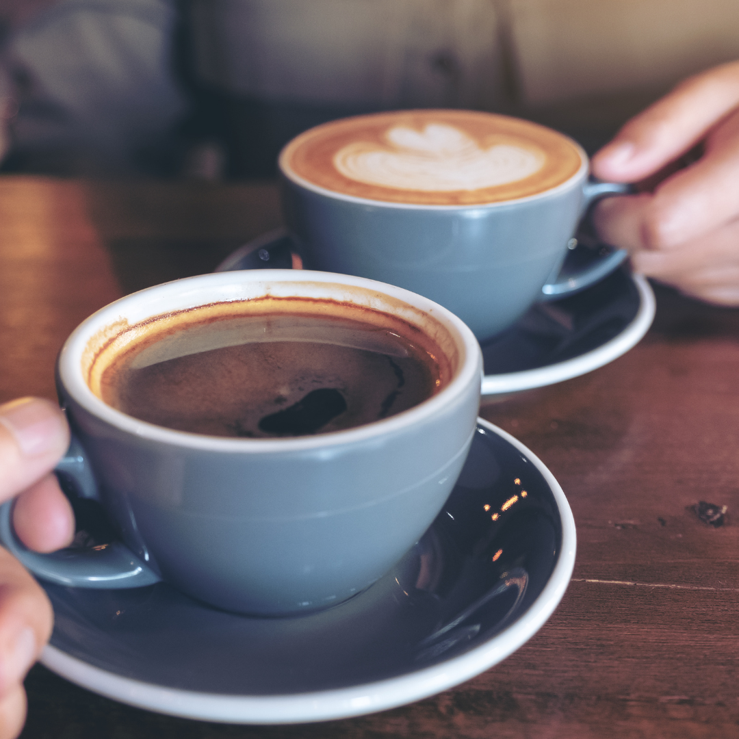 Two cups of coffee on a wooden table, one black coffee and one latte with foam art