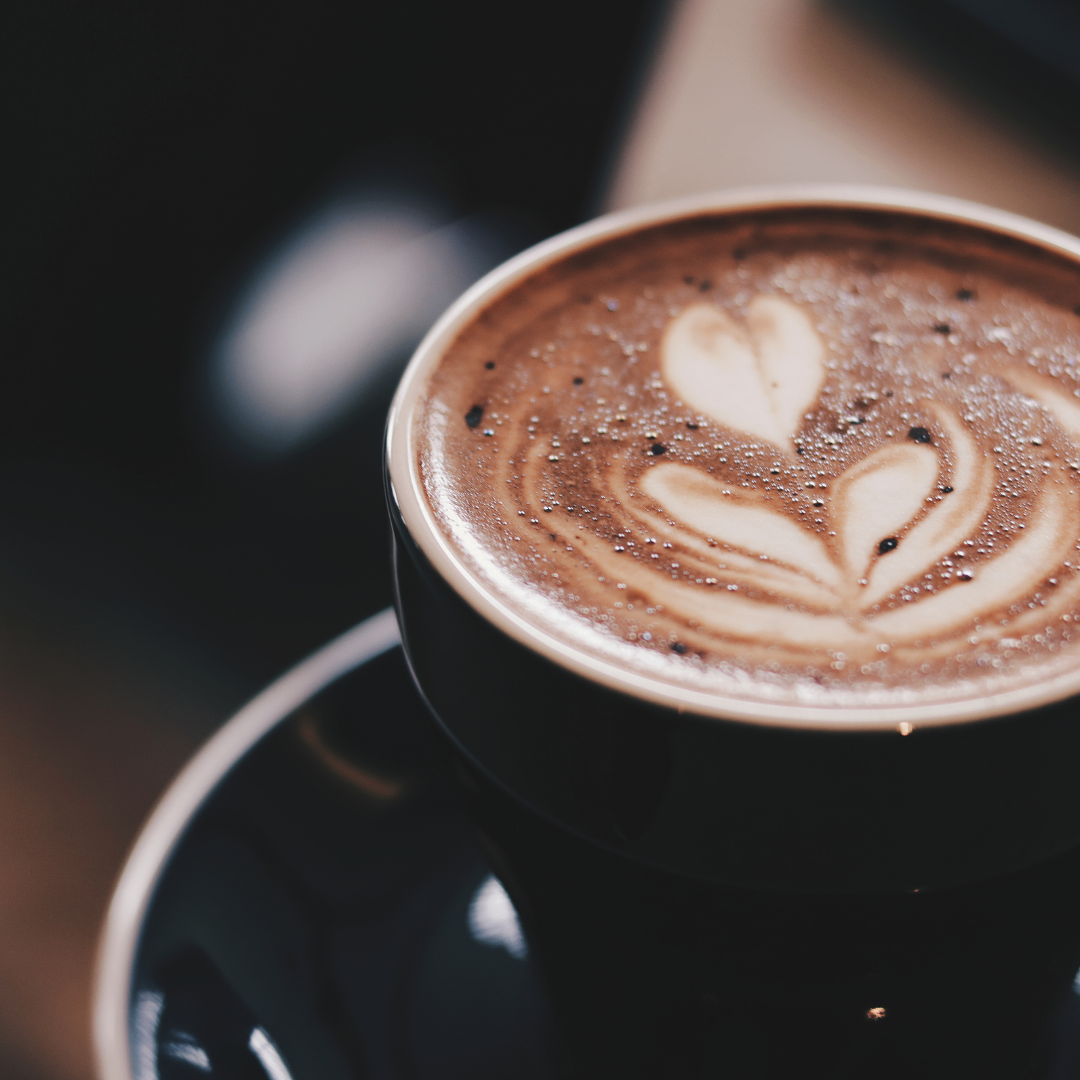 Close up of a dark roast latte in a black cup with heart shaped latte art on creamy foam