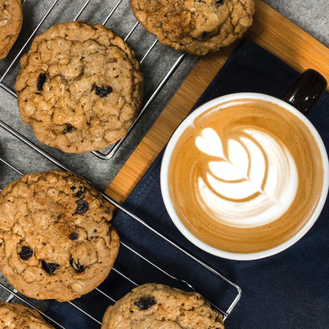 Latte with leaf latte art next to chocolate chip cookies on cooling racks