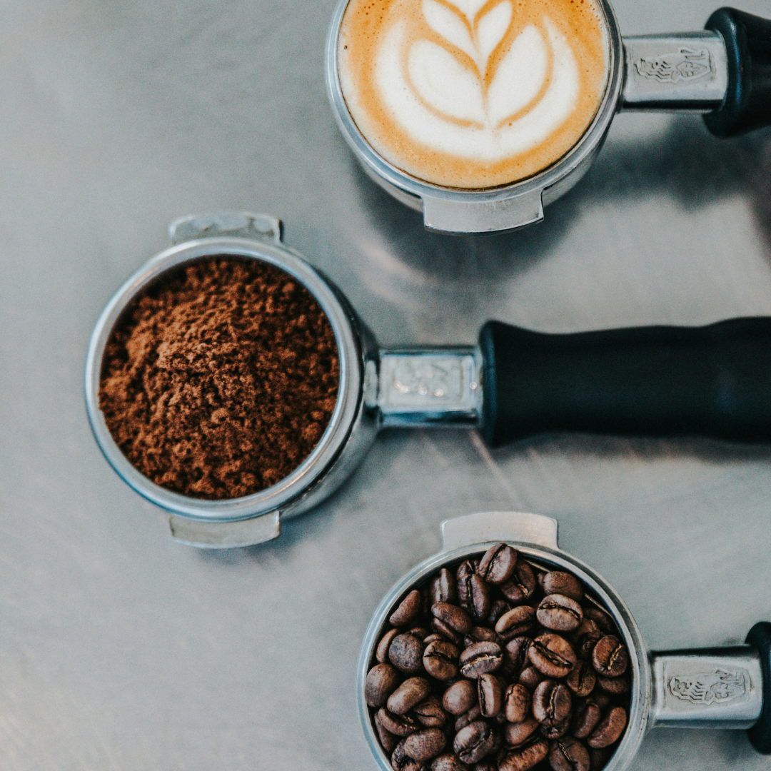 Top view of espresso portafilters with ground coffee, whole beans, and a latte with leaf latte art.