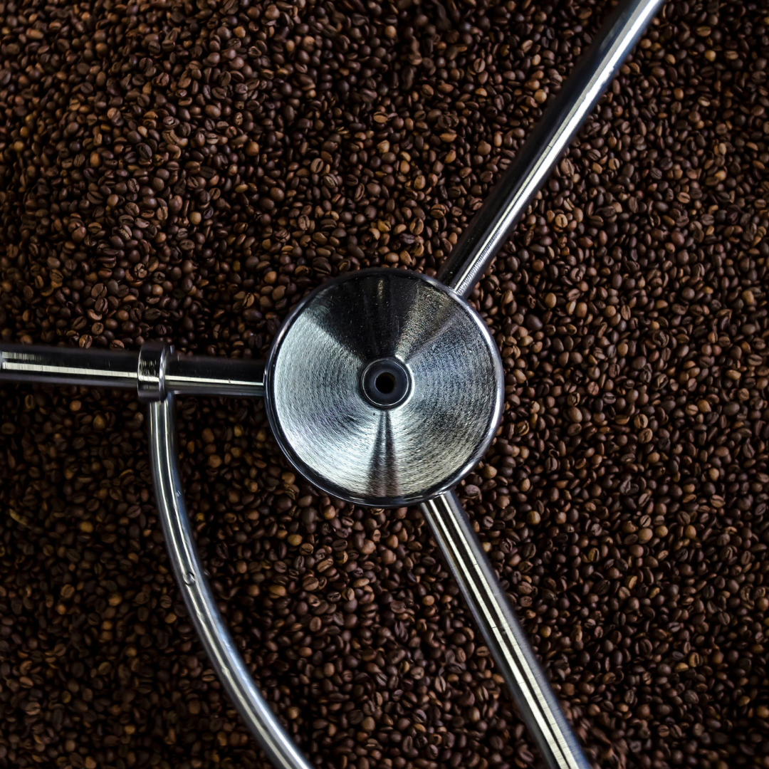 Close-up of freshly roasted coffee beans filling a roasting drum with a metal stirring arm visible from above