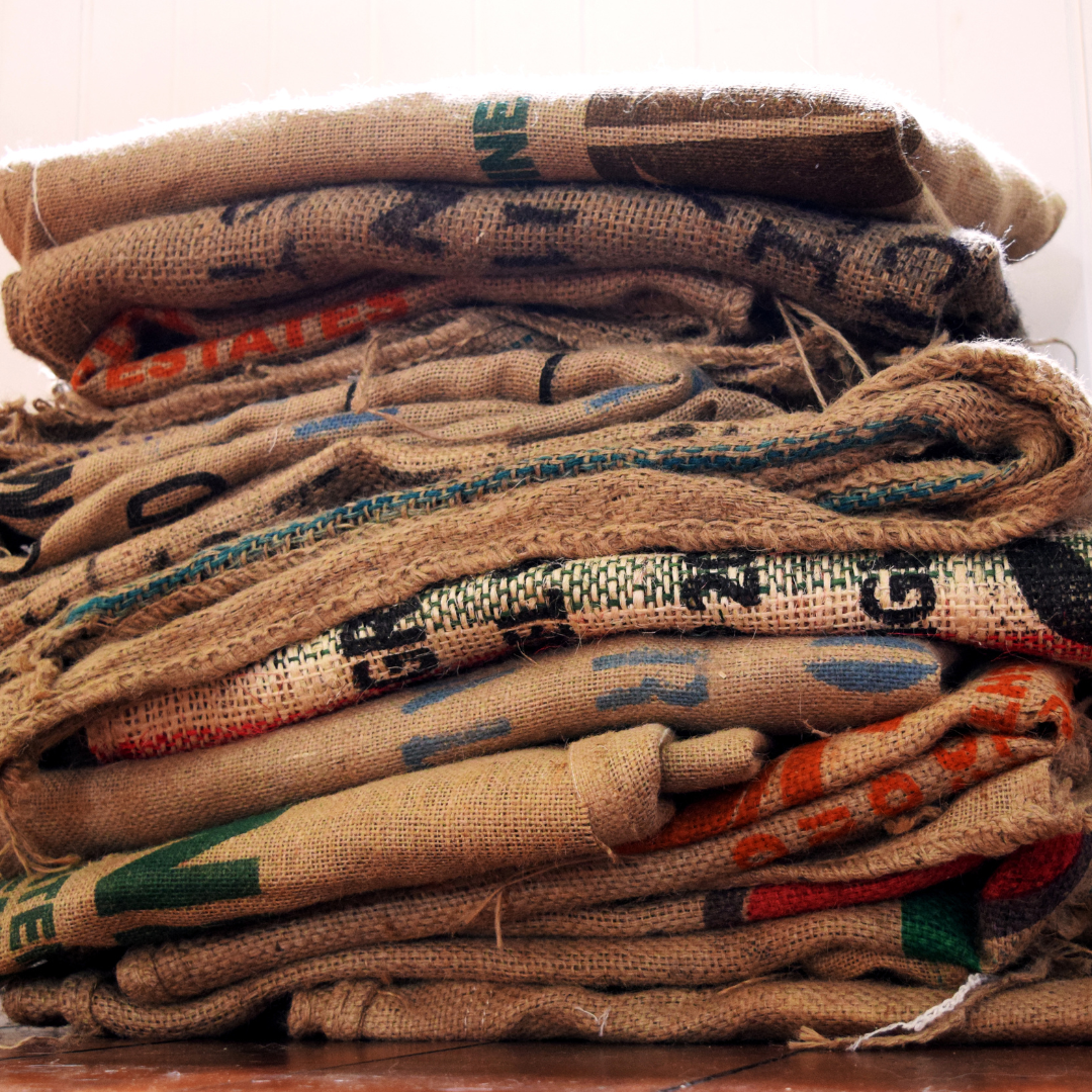 Stacked burlap coffee sacks with printed origin markings, folded and layered on a wooden surface, highlighting raw green coffee storage and global sourcing.