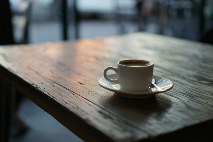White espresso cup filled with coffee on a matching saucer, placed on a worn wooden café table with a softly blurred background.