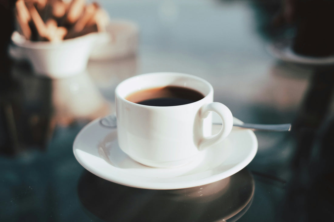 White cup of freshly brewed black coffee on a saucer, placed on a glossy café table with a softly blurred background