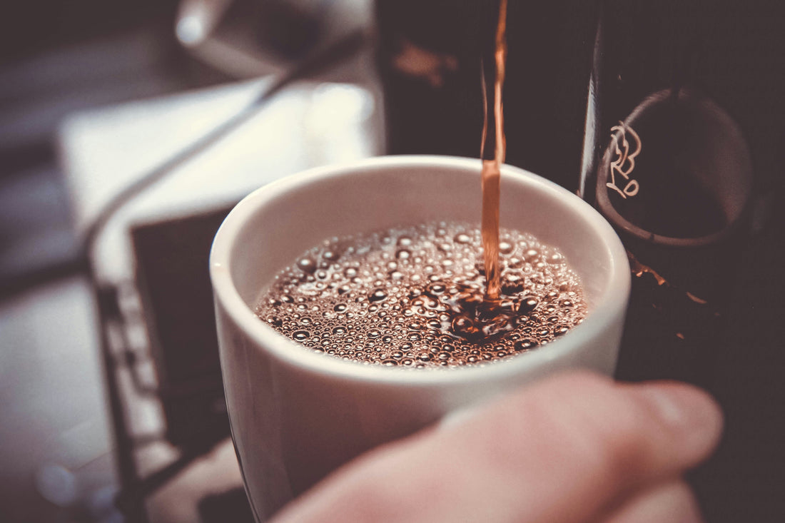Stream of freshly brewed coffee pouring into a white mug, creating a layer of bubbles as it fills
