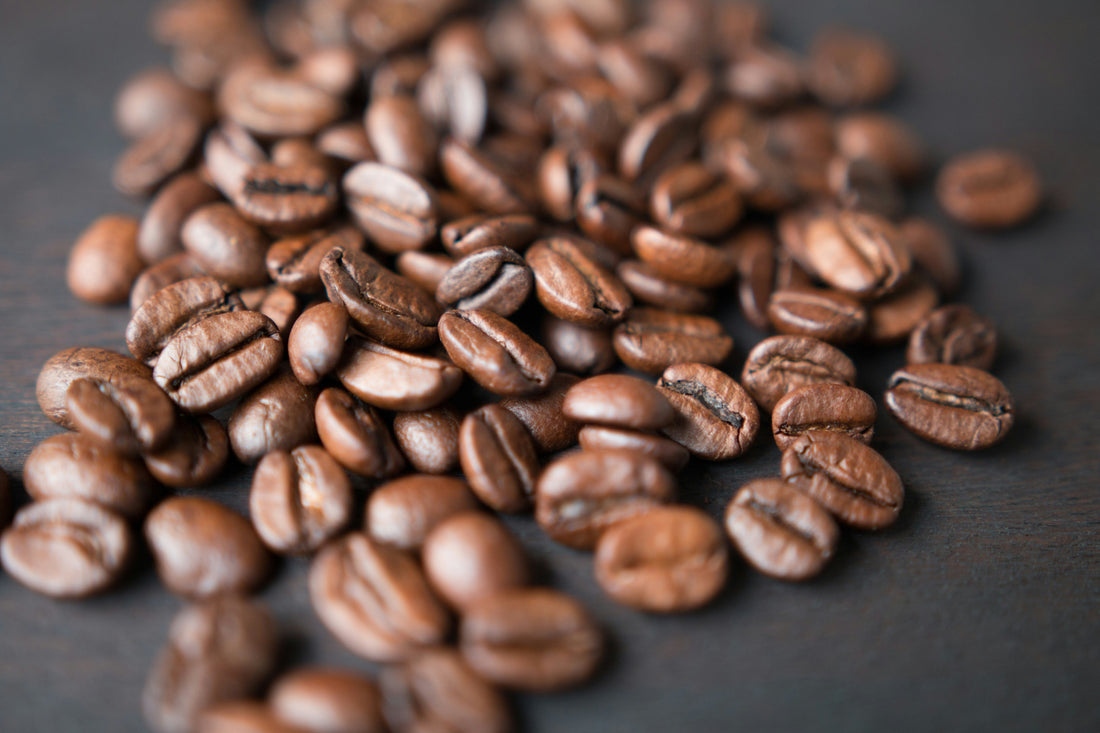 Close-up of roasted coffee beans scattered across a dark surface