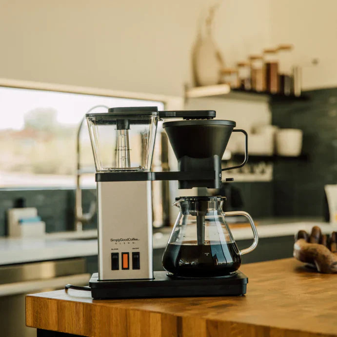 Automatic pour-over coffee maker with a glass carafe on a wooden kitchen counter