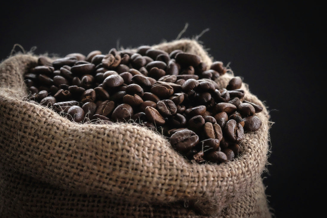 Close-up of roasted coffee beans overflowing from a burlap sack against a dark background