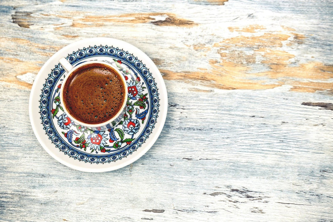 Overhead view of a freshly brewed cup of coffee on a colorful patterned saucer, placed on a rustic whitewashed wooden surface