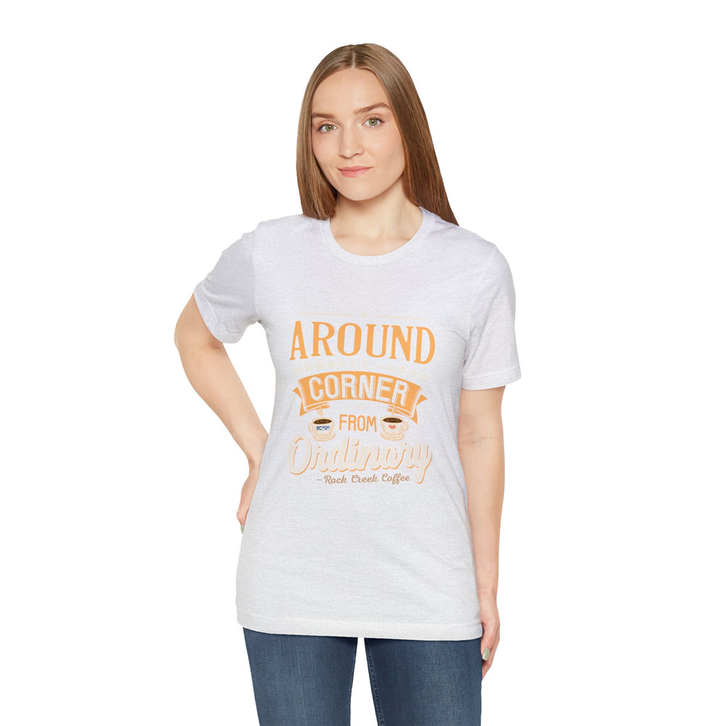 Female model wearing an ash Rock Creek Coffee T-shirt featuring the “Around the Corner From Ordinary” graphic print