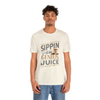 Adult man modeling a cream short-sleeve T-shirt printed with the phrase “Sippin on Genius Juice” in a bold coffee-themed graphic with a small coffee cup illustration, shown against a plain white background.