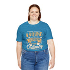 Adult woman smiling while modeling an aqua short-sleeve T-shirt featuring the “Around the Corner from Ordinary” graphic in a bold coffee-themed typographic design, shown against a plain white background.