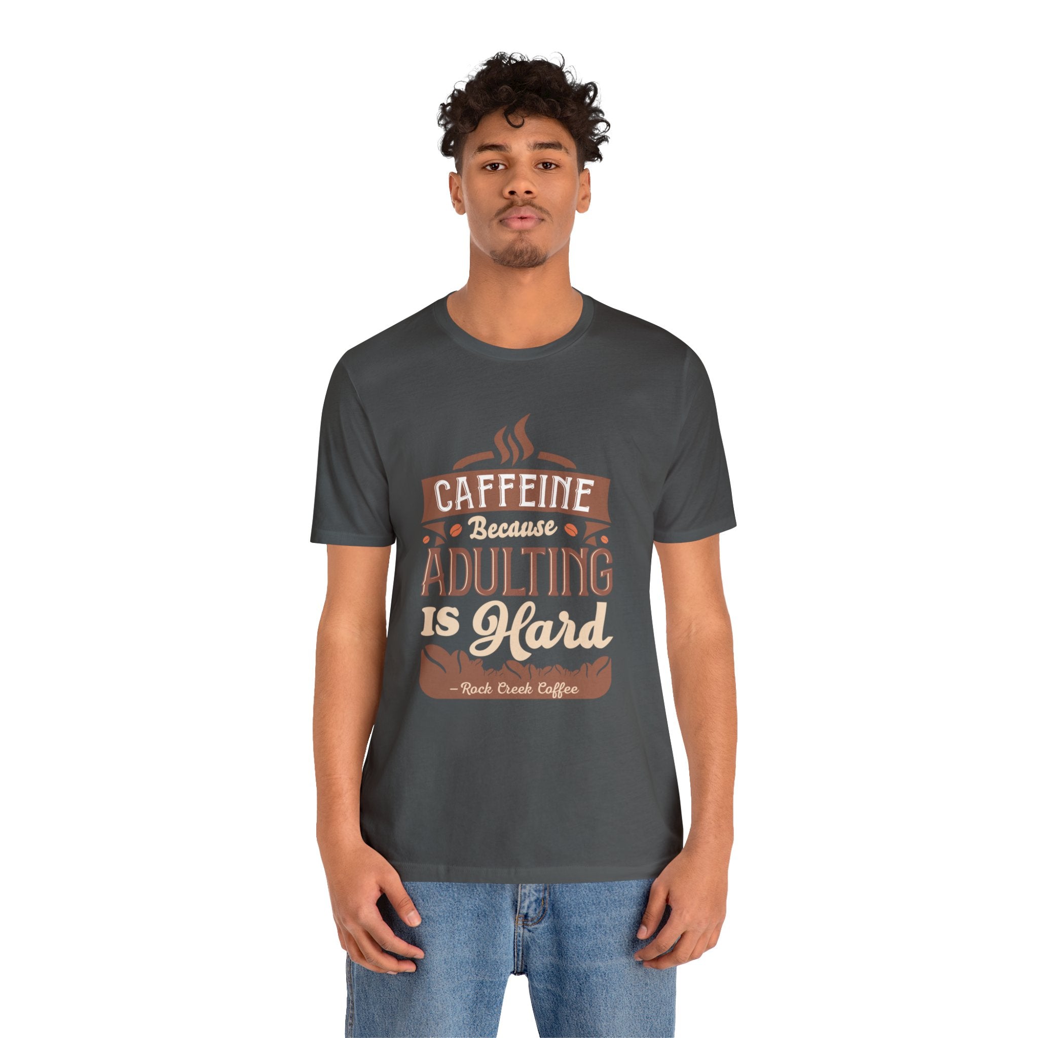 Adult man modeling an asphalt short-sleeve T-shirt featuring the “Caffeine Because Adulting Is Hard” graphic in a stacked typographic design, shown against a plain white background.