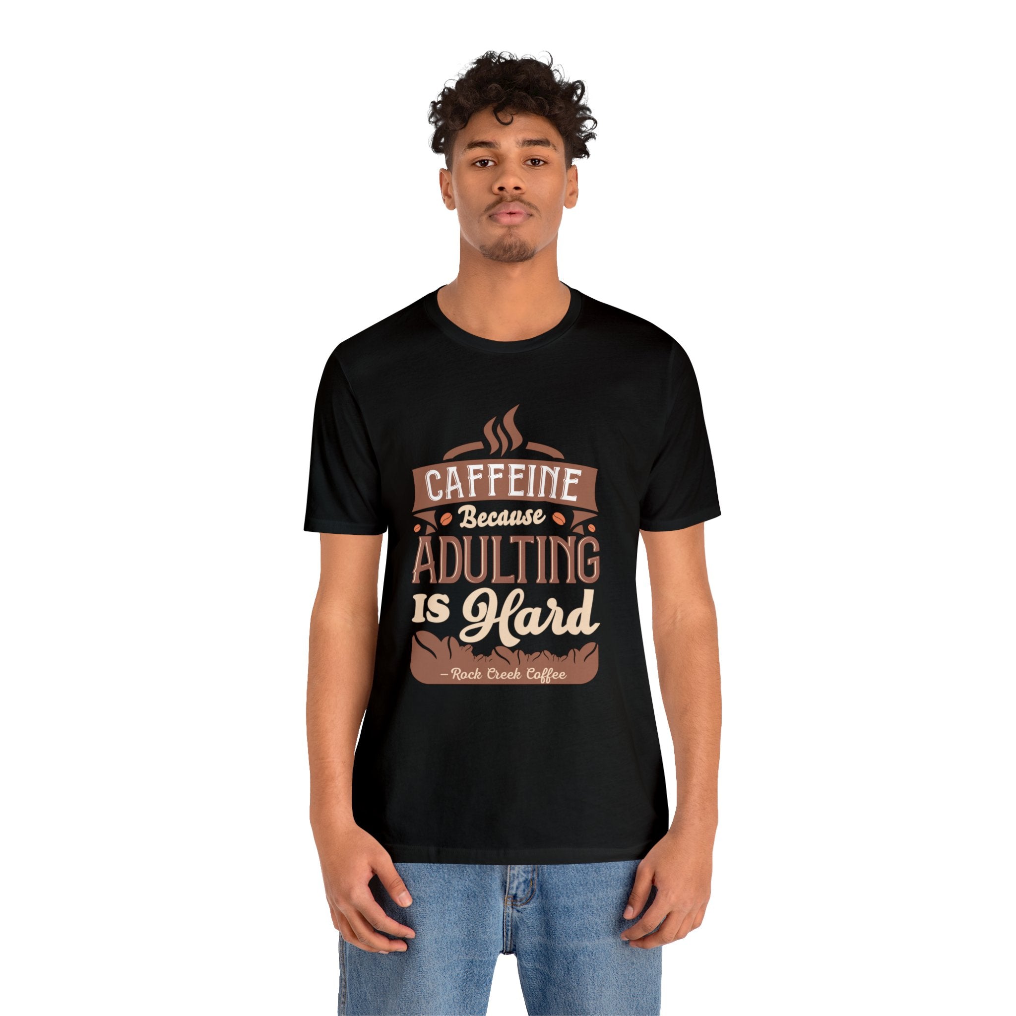 Adult man modeling a black short-sleeve T-shirt featuring the “Caffeine Because Adulting Is Hard” graphic in a stacked typographic design, shown against a plain white background.