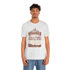 Adult man and woman modeling matching soft cream short-sleeve T-shirts featuring the “Caffeine Because Adulting Is Hard” graphic in a stacked typographic design, posed together against a plain white background.