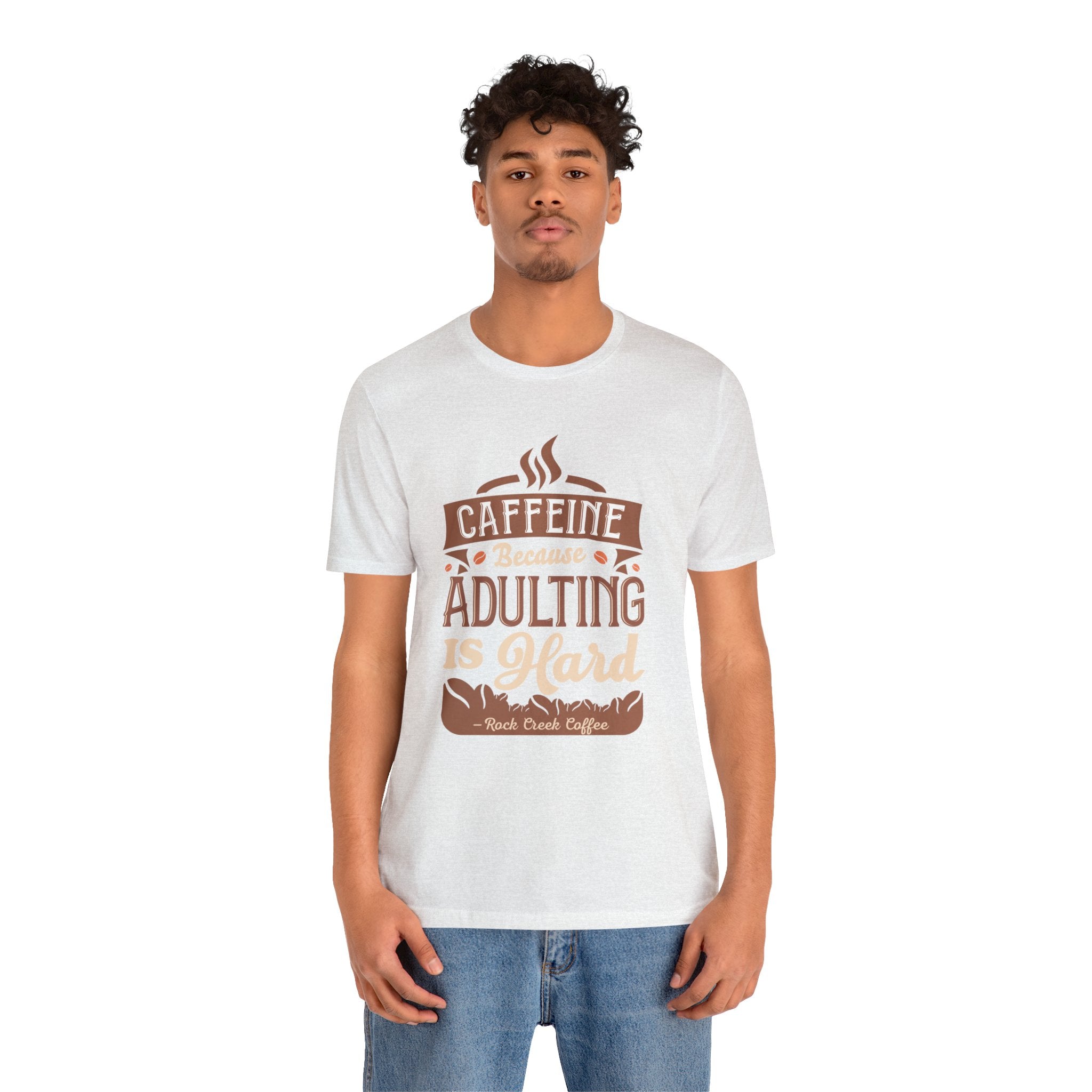 Adult man and woman modeling matching soft cream short-sleeve T-shirts featuring the “Caffeine Because Adulting Is Hard” graphic in a stacked typographic design, posed together against a plain white background.