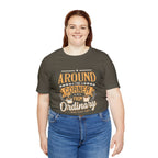 Adult woman smiling while modeling an army green short-sleeve T-shirt featuring the “Around the Corner from Ordinary” graphic in a bold coffee-themed typographic design, shown against a plain white background.