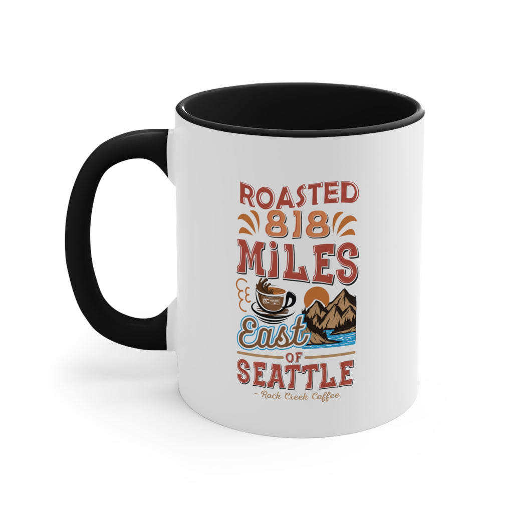 White ceramic coffee mug with black handle and black interior featuring the Roasted 818 Miles East of Seattle Rock Creek Coffee design with coffee cup and mountain illustration.