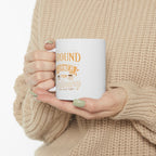 Person wearing a beige knit sweater holding a white Rock Creek Coffee mug with “Around the Corner from Ordinary” design in gold and cream lettering.