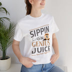 Adult woman modeling a white short-sleeve T-shirt featuring the “Sippin on Genius Juice” graphic in bold coffee-inspired lettering with a small mug illustration, photographed indoors beside a potted plant against a light background.