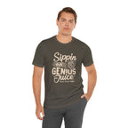 Adult man modeling an olive green short-sleeve T-shirt printed with the slogan “Sippin on Genius Juice” and a stylized coffee to-go cup graphic on the front, shown against a white background.