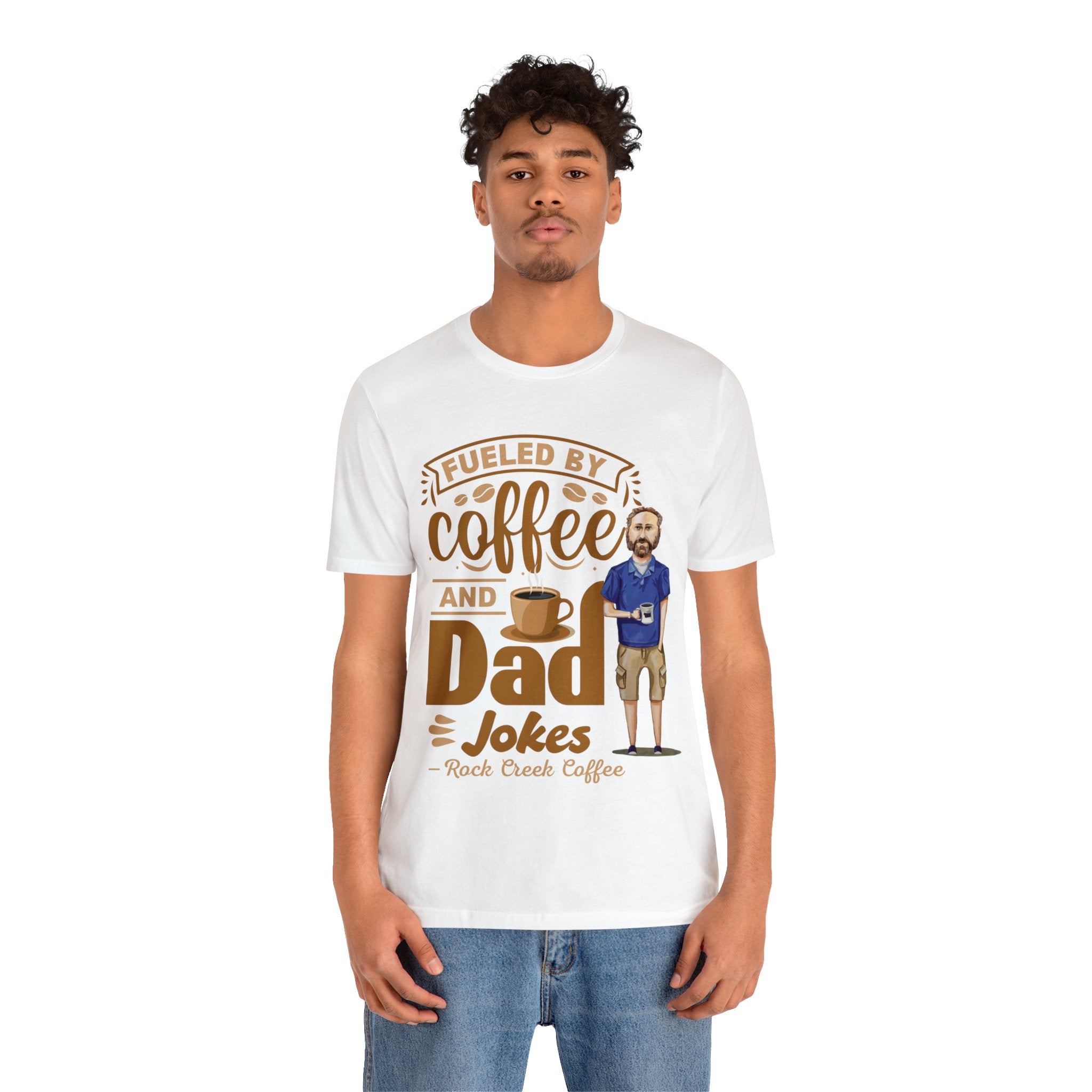 Man modeling a white graphic T-shirt featuring the phrase “Fueled by Coffee and Dad Jokes” with a coffee cup illustration and cartoon dad character on the front.