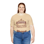 Adult woman smiling while modeling a soft cream short-sleeve T-shirt featuring the “Caffeine Because Adulting Is Hard” graphic in a stacked typographic design, shown against a plain white background.
