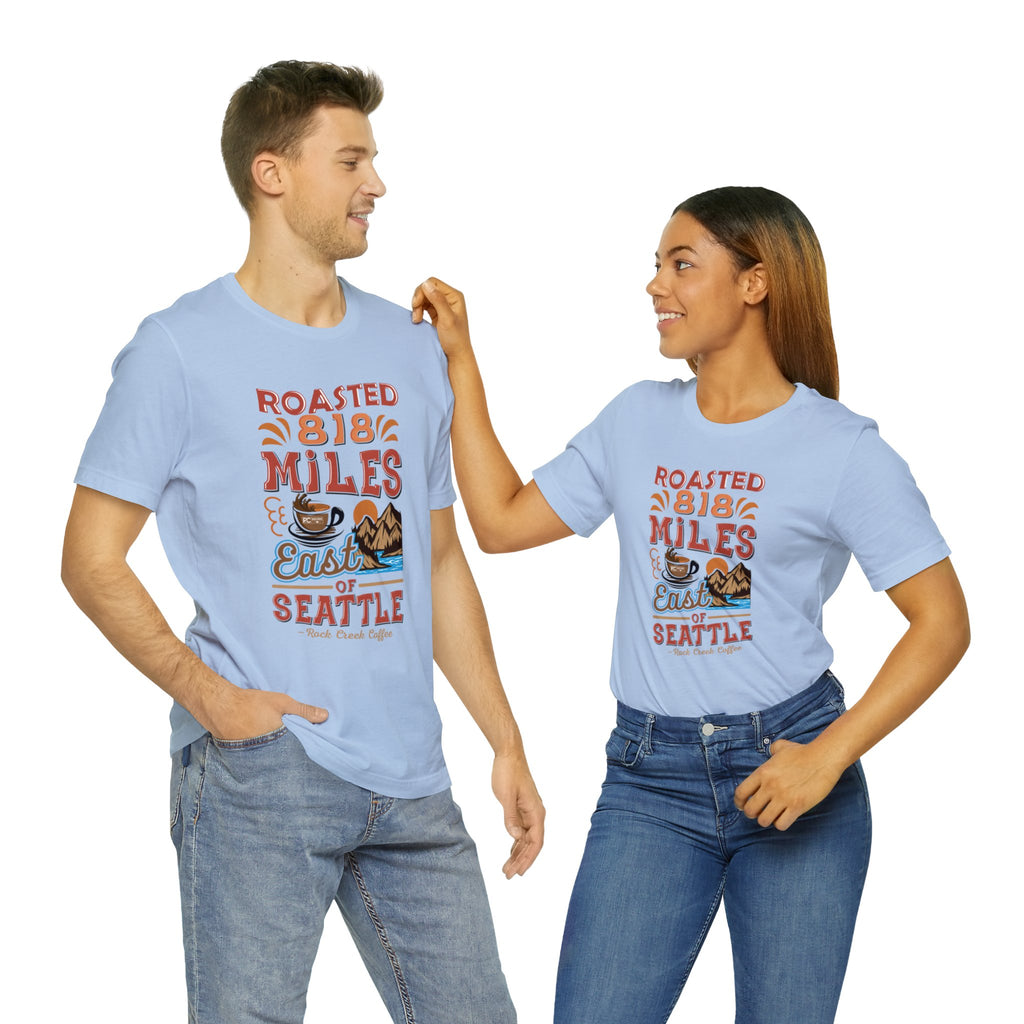 Adult man and woman modeling matching light blue Seattle coffee graphic T-shirts reading “Roasted 818 Miles East of Seattle,” shown against a plain white background.