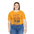 Adult woman modeling a golden yellow short-sleeve T-shirt printed with a colorful graphic that reads “Roasted 818 Miles East of Seattle,” featuring a steaming coffee cup and mountain lake illustration, shown against a plain white background.