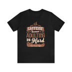 Black short-sleeve T-shirt displayed flat against a plain white background, featuring the phrase “Caffeine Because Adulting Is Hard” in a stacked typographic design with Rock Creek Coffee branding below.