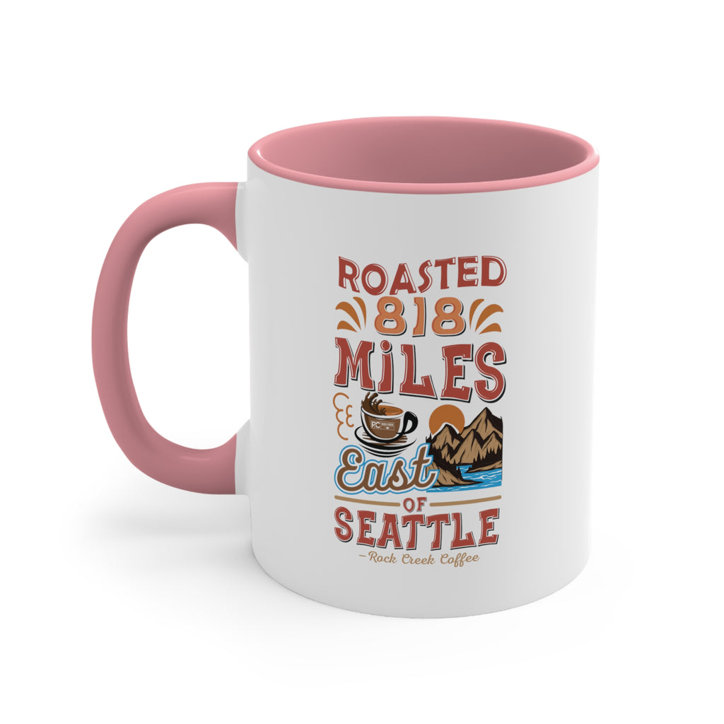 White ceramic coffee mug with pink handle and pink interior featuring the Roasted 818 Miles East of Seattle Rock Creek Coffee design with coffee cup and mountain illustration.