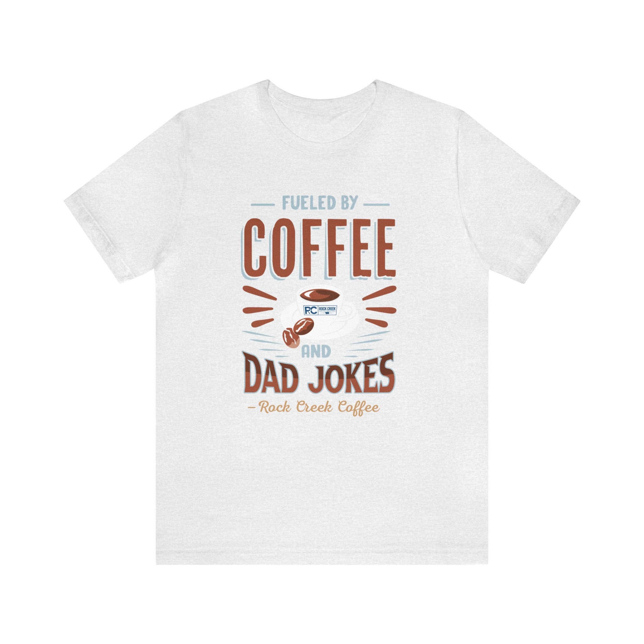 Ash short-sleeve T-shirt displayed flat against a plain white background, featuring the “Fueled by Coffee and Dad Jokes” graphic with a coffee cup illustration and Rock Creek Coffee text below.