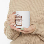 White Rock Creek Coffee mug featuring the phrase “Caffeine Because Adulting Is Hard” in brown and tan lettering, held by a person wearing a beige knit sweater with green painted nails against a plain white background.