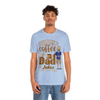 Young man modeling a light blue T-shirt with a coffee-themed graphic reading “Fueled by Coffee and Dad Jokes” featuring a steaming coffee cup and cartoon dad illustration on the front.
