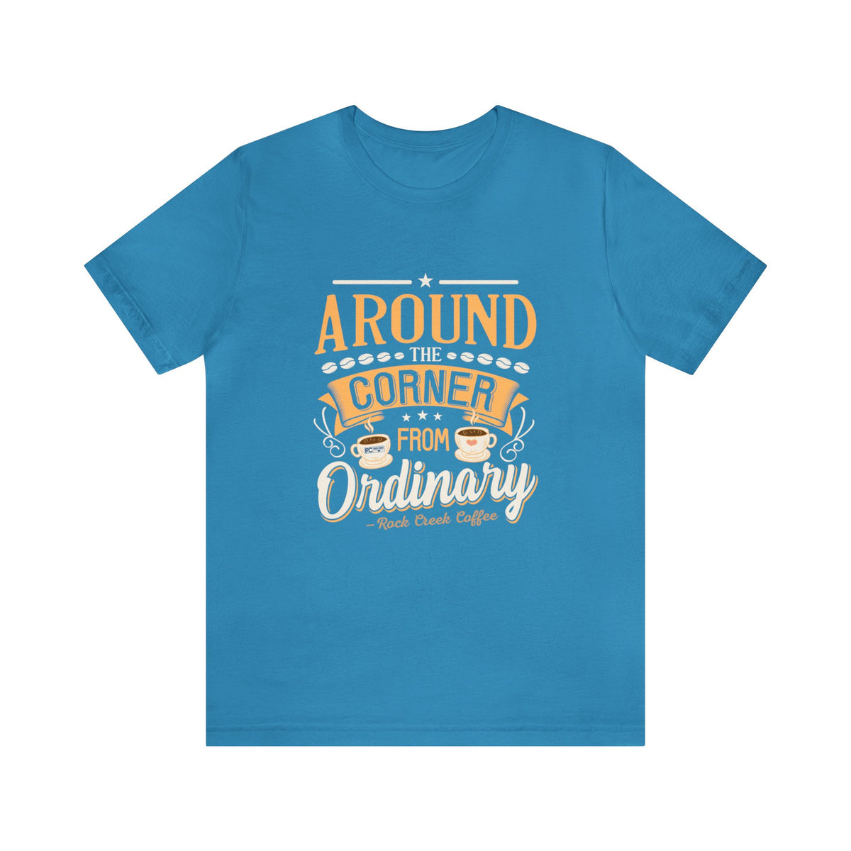 Aqua short-sleeve T-shirt displayed flat against a plain white background, featuring the phrase “Around the Corner from Ordinary” in a bold coffee-themed typographic design with Rock Creek Coffee branding below.