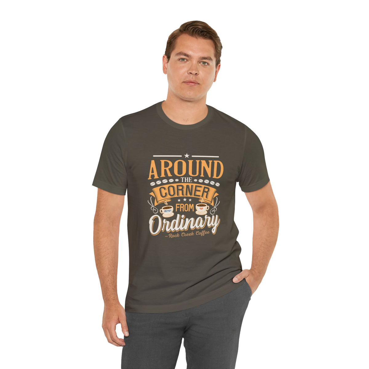 Adult man modeling an army green short-sleeve T-shirt featuring the “Around the Corner from Ordinary” graphic in a bold coffee-themed typographic design, posed with one hand in his pocket against a plain white background.
