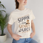 Lifestyle image of an adult woman wearing a cream short-sleeve T-shirt with the “Sippin on Genius Juice” graphic, featuring bold coffee-inspired lettering and a small cup illustration, photographed indoors beside a potted plant.