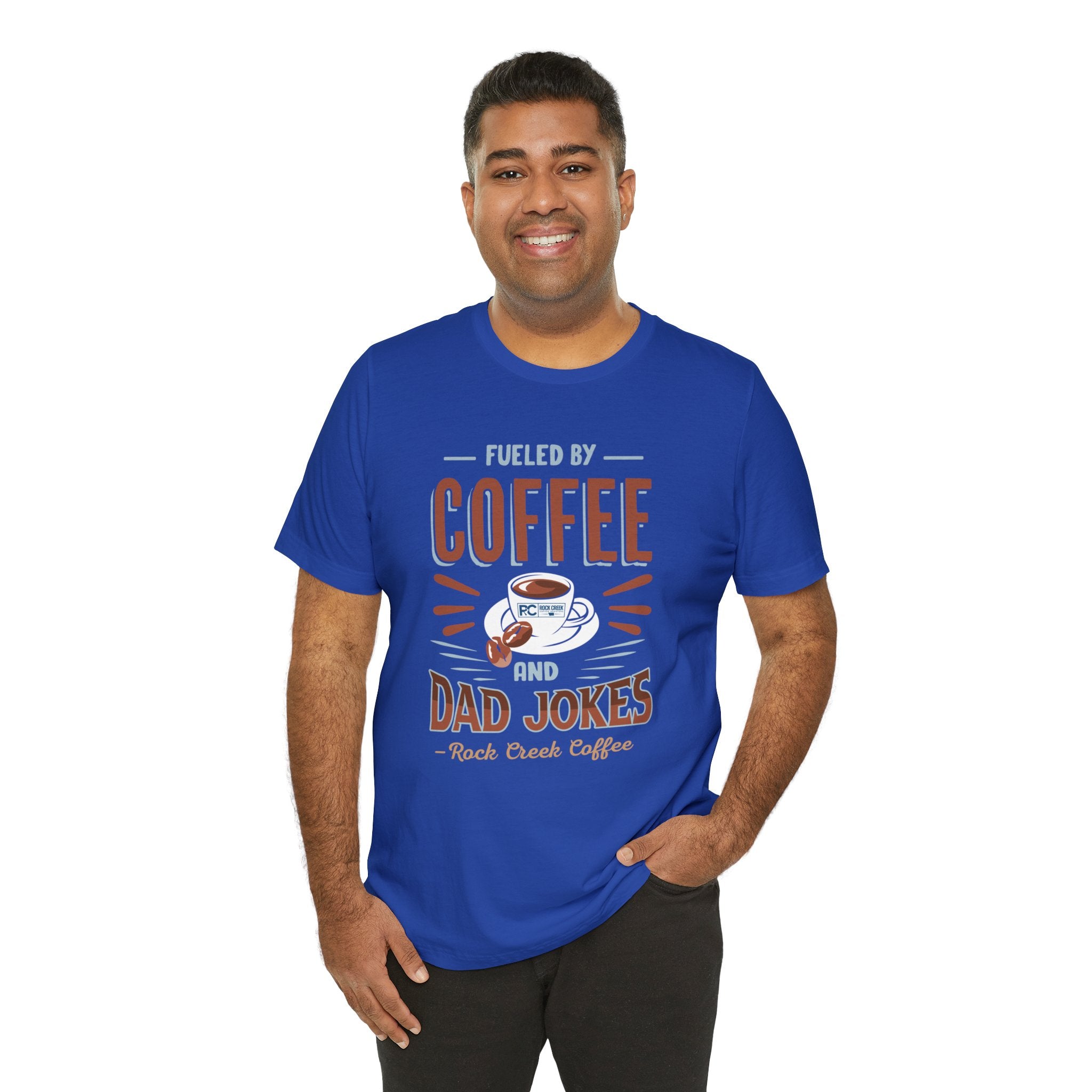 Adult man smiling while modeling a royal blue short-sleeve T-shirt printed with a bold graphic that reads “Fueled by Coffee and Dad Jokes,” featuring a coffee cup illustration, shown against a plain white background.