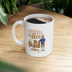 White ceramic coffee mug filled with coffee featuring the text Fueled by Coffee and Dad Jokes Rock Creek Coffee with a cartoon illustration of a man holding a coffee cup, placed on a wooden table with green plants in the background.