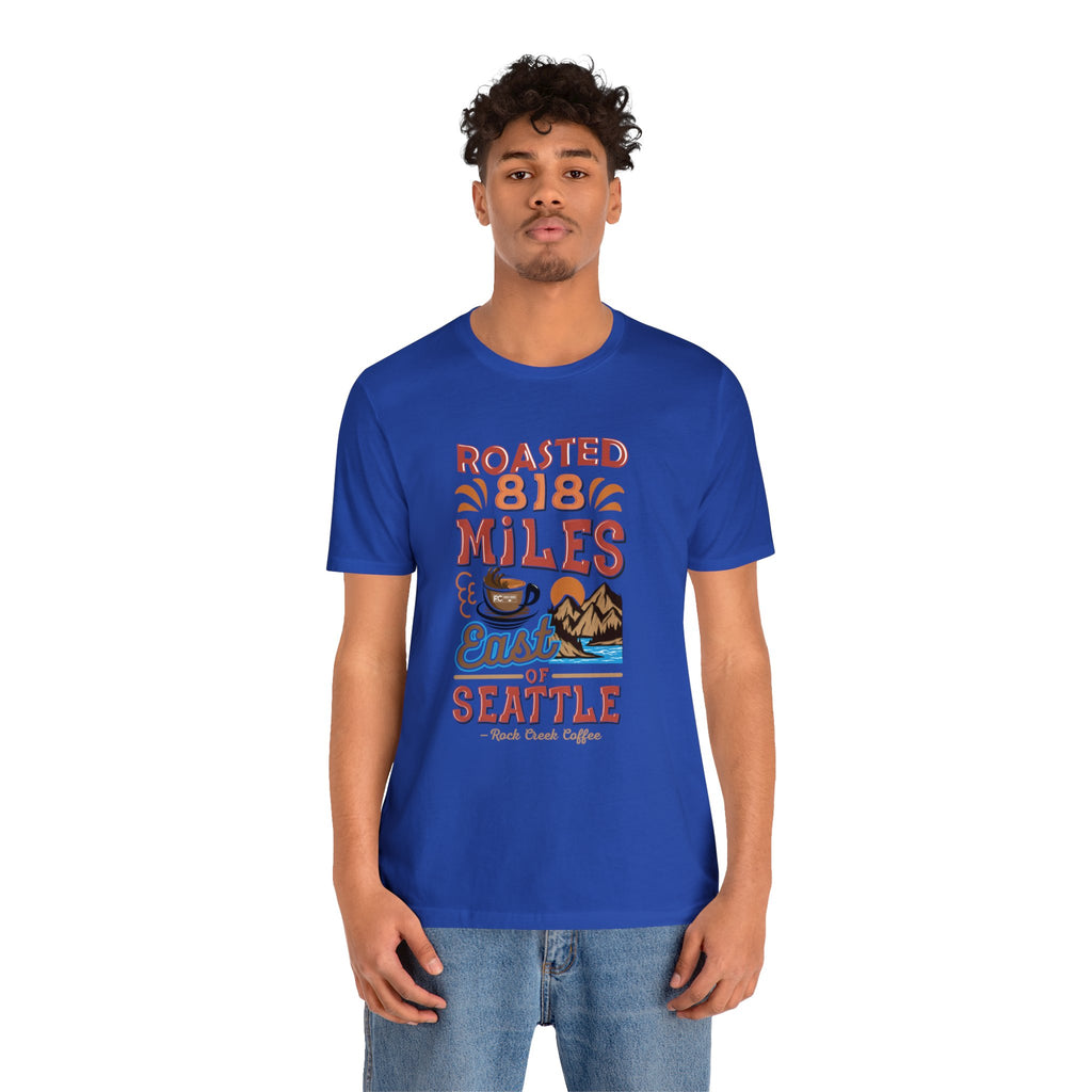 Men’s royal blue Seattle coffee graphic T-shirt reading “Roasted 818 Miles East of Seattle,” shown on a model against a white background.
