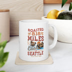 White Rock Creek Coffee mug featuring the colorful “Roasted 818 Miles East of Seattle” design, displayed on a kitchen counter with a bowl of lemons and avocados in the background.