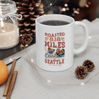 White Rock Creek Coffee mug with a colorful “Roasted 818 Miles East of Seattle” design, filled with hot coffee and styled with pinecones, a candle, cinnamon sticks, and warm string lights in a cozy setting.