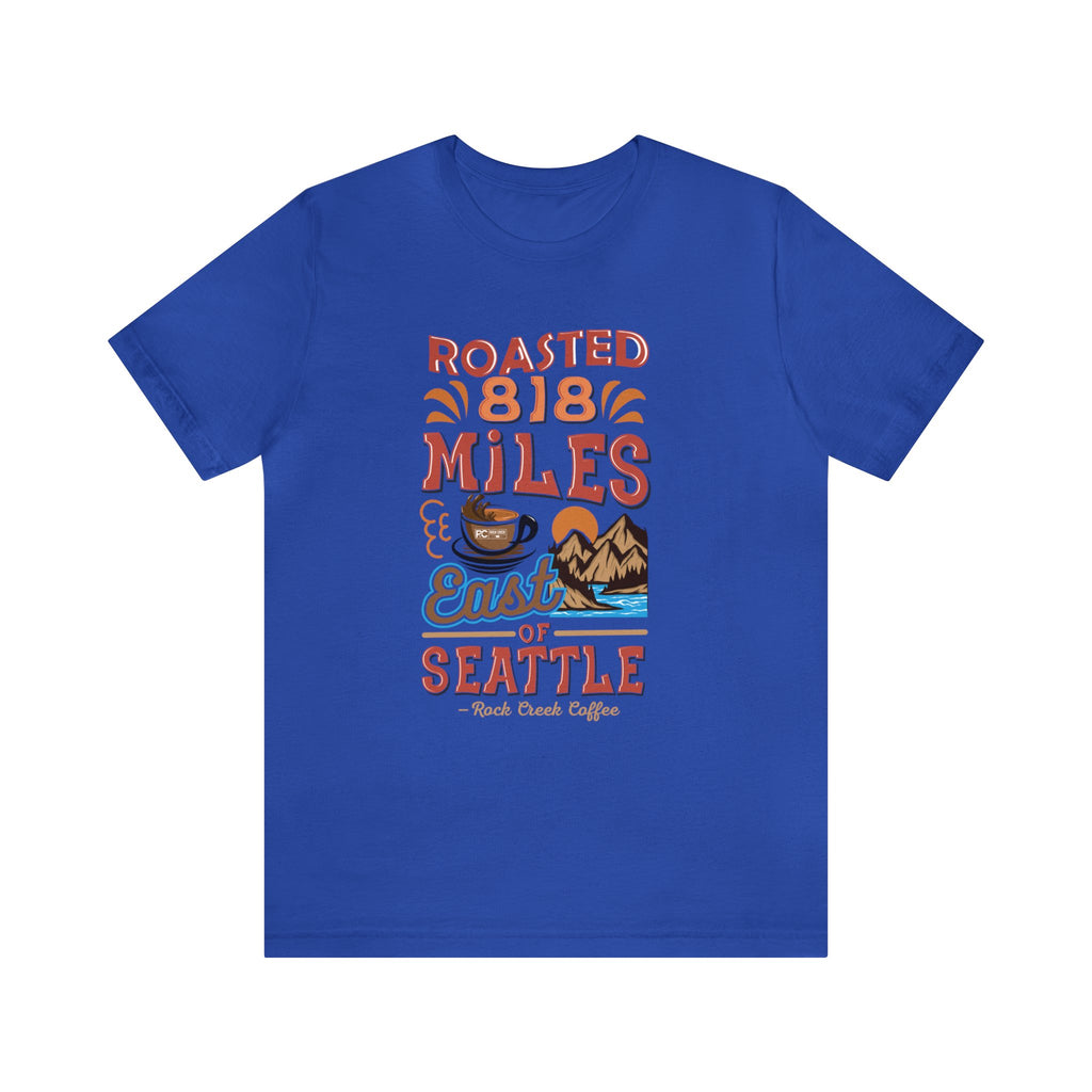 Royal blue Seattle coffee graphic T-shirt with “Roasted 818 Miles East of Seattle” print and scenic coffee illustration, shown on a white background.