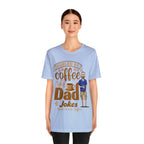 Woman modeling a light blue graphic T-shirt featuring the phrase “Fueled by Coffee and Dad Jokes” with a steaming coffee cup icon and cartoon dad illustration on the front, against a plain white background.