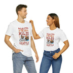 Smiling man and woman standing side by side, both wearing white short-sleeve T-shirts printed with a colorful coffee-themed graphic reading “Roasted 818 Miles East of Seattle,” featuring a steaming coffee cup and scenic mountain–lake illustration, shown against a plain white background.