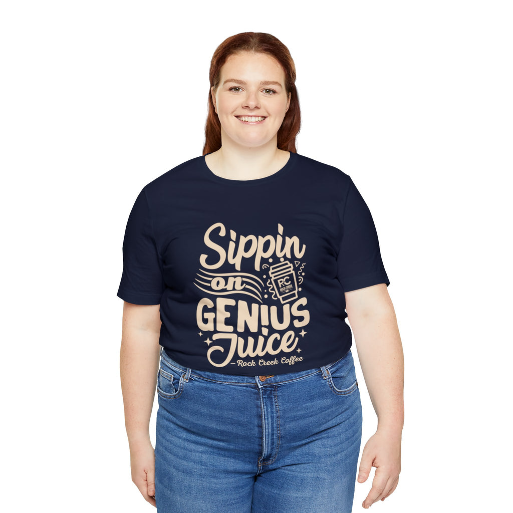 Smiling woman modeling a navy short-sleeve T-shirt printed with the slogan “Sippin on Genius Juice” and a stylized coffee to-go cup graphic on the front, shown against a plain white background.