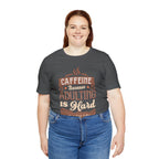 Adult woman smiling while modeling an asphalt short-sleeve T-shirt featuring the “Caffeine Because Adulting Is Hard” graphic in a stacked typographic design, shown against a plain white background.