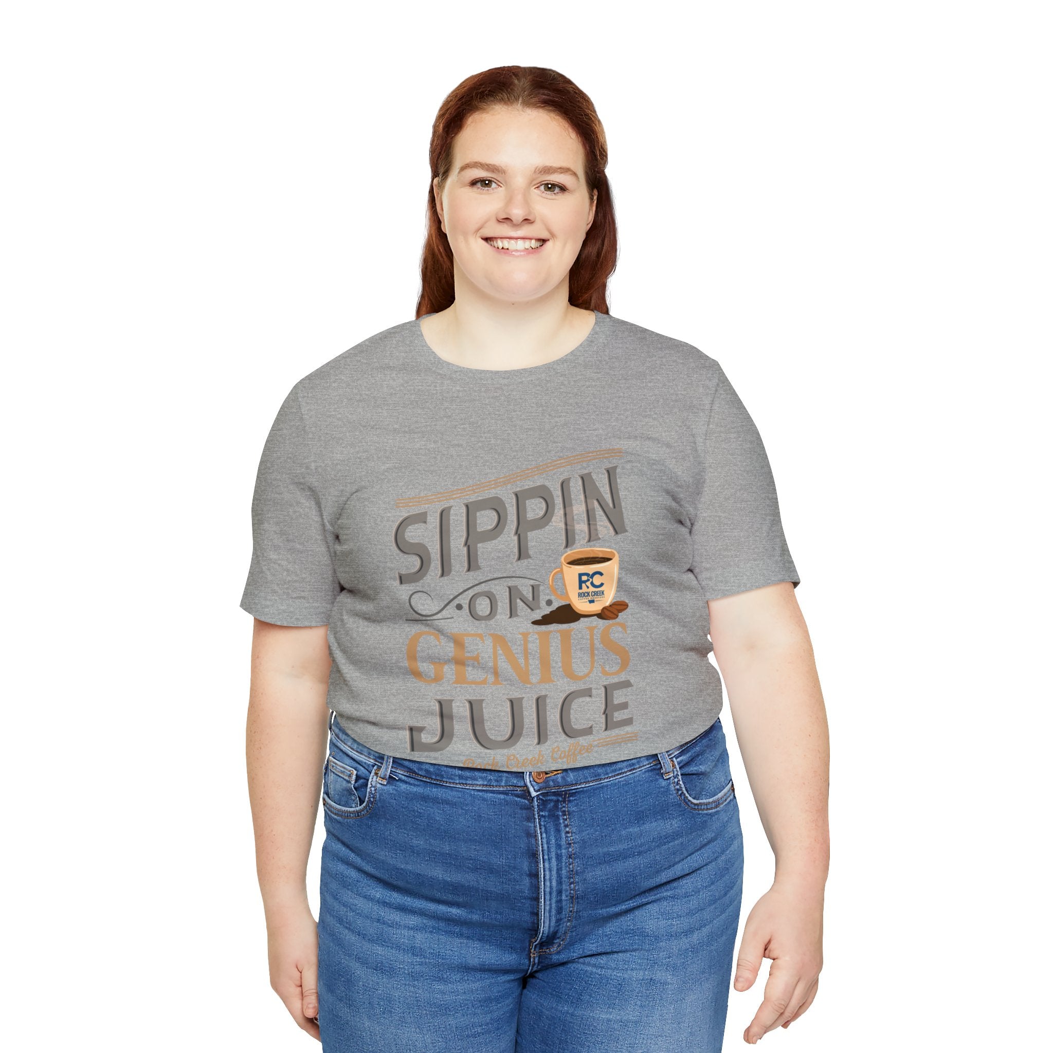 Adult woman smiling while modeling a heather gray short-sleeve T-shirt featuring the “Sippin on Genius Juice” graphic in bold coffee-inspired lettering, photographed against a plain white background.