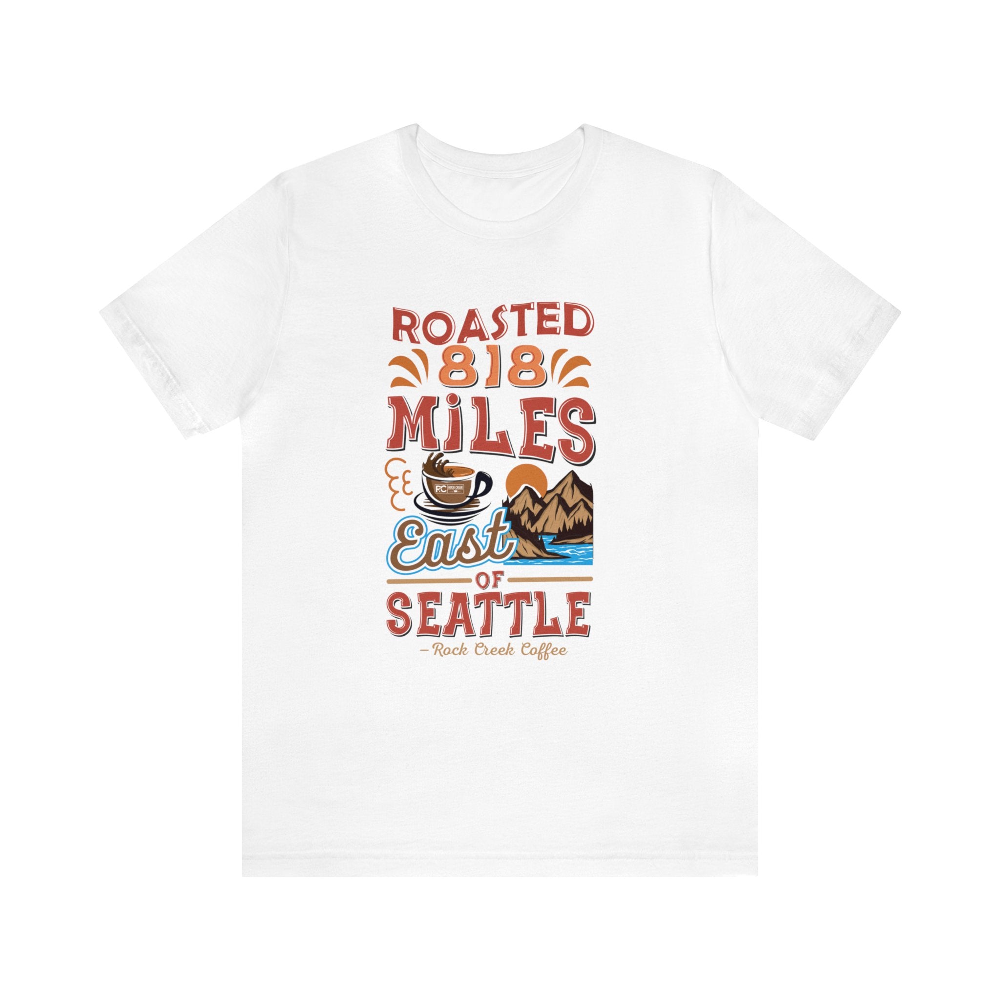 White short-sleeve T-shirt displayed flat against a white background featuring a colorful graphic that reads “Roasted 818 Miles East of Seattle” with a steaming coffee cup and mountain lake scene illustration on the front.