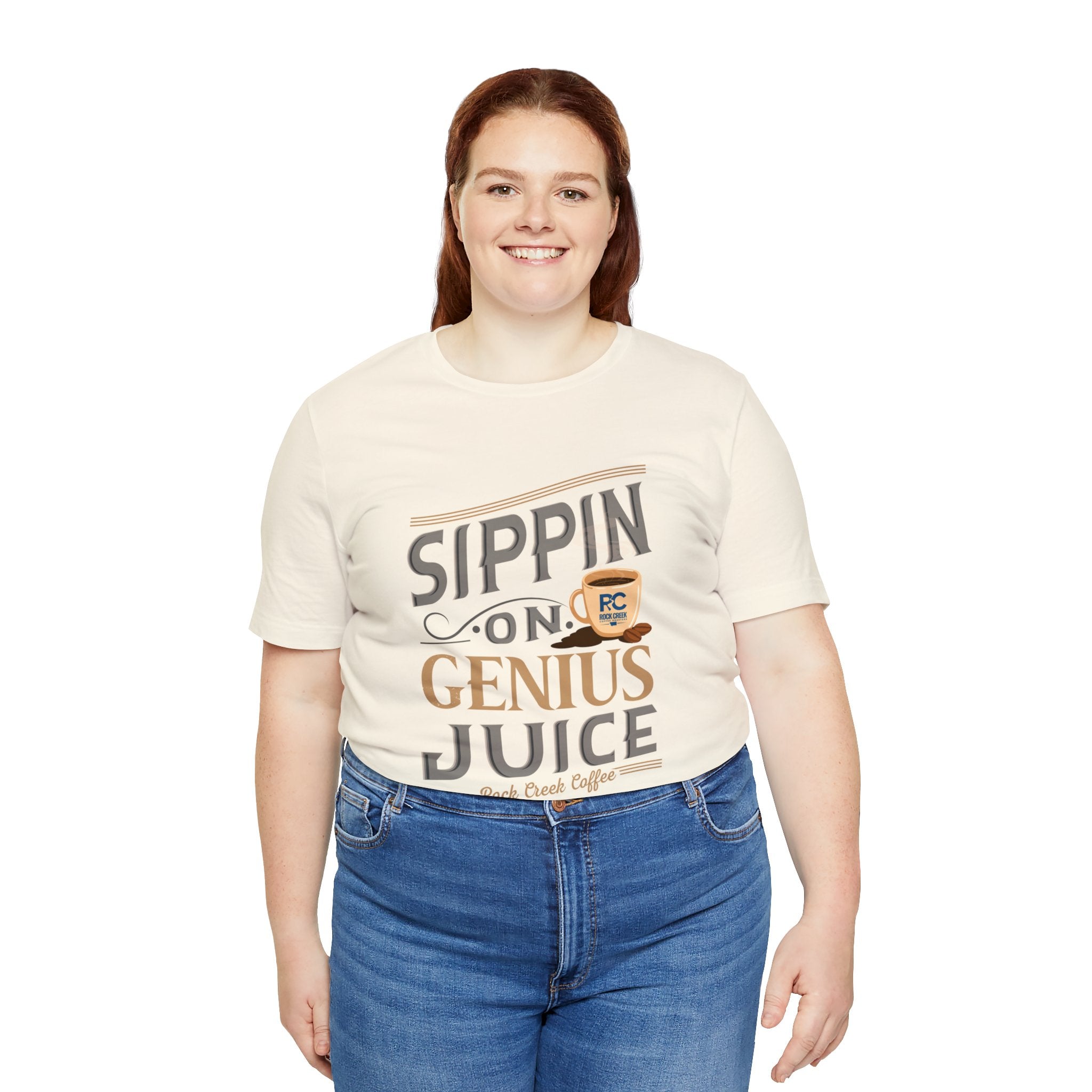Adult woman smiling while wearing a cream short-sleeve T-shirt printed with the “Sippin on Genius Juice” graphic in large coffee-inspired lettering, photographed against a plain white background.